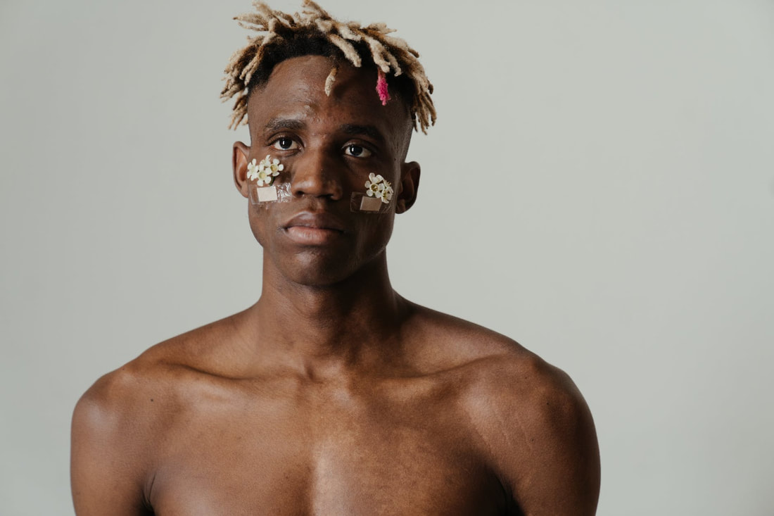 Black masculine-presenting person with flowers taped to their face with bandages.